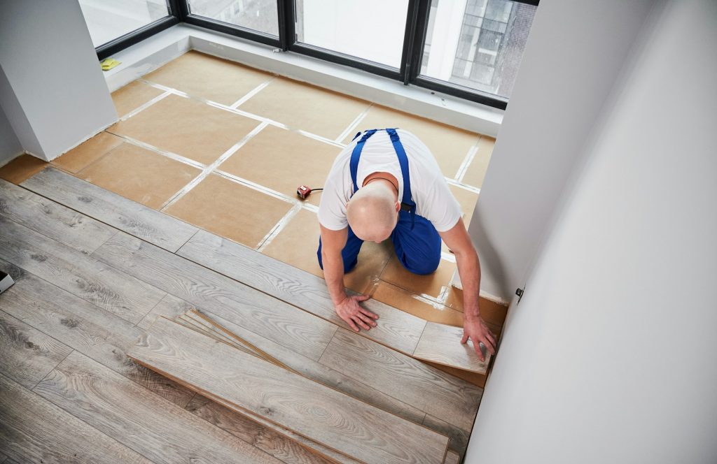 Man laying laminate flooring in apartment under renovation.